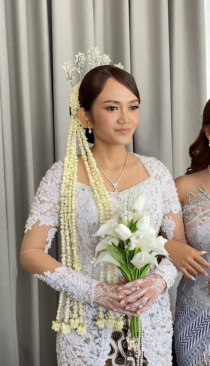 Pengantin berkebaya putih dengan ronce melati dan buket bunga lili