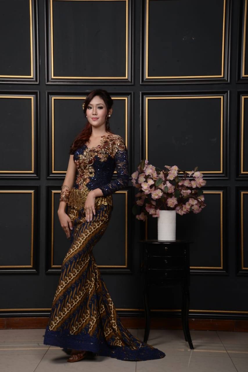 Kebaya dengan rok duyung batik sogan di depan dinding panel gelap