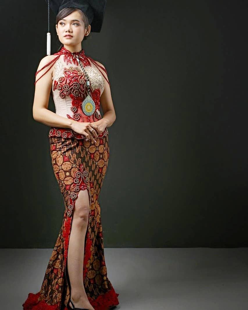 Kebaya halter merah dengan rok duyung batik merah cokelat, dipakai bersama topi toga