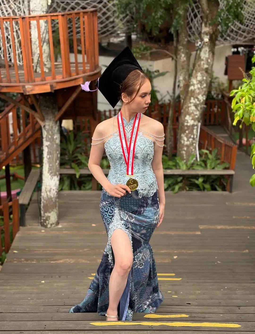 Kebaya biru dengan rok duyung berbelahan, wisudawati memakai topi toga