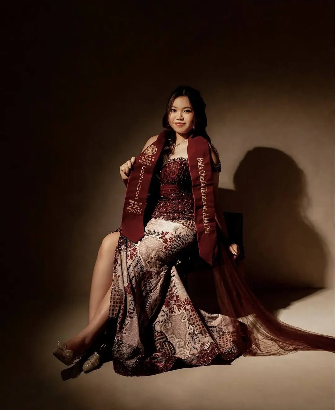 Kebaya off-shoulder marun berpayet dengan selendang tile menjuntai