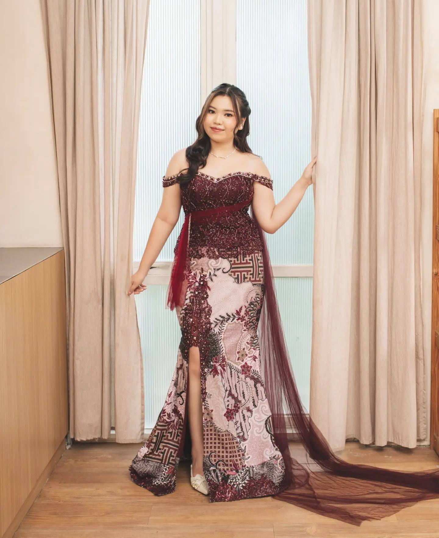 Kebaya marun off-shoulder dengan rok batik berbelahan dan selendang tile
